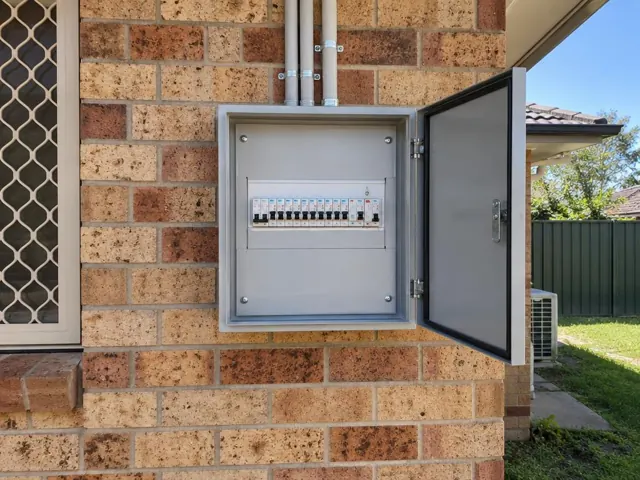 Outdoor electrical switchboard mounted on a brick home wall with the door open in Aberglasslyn